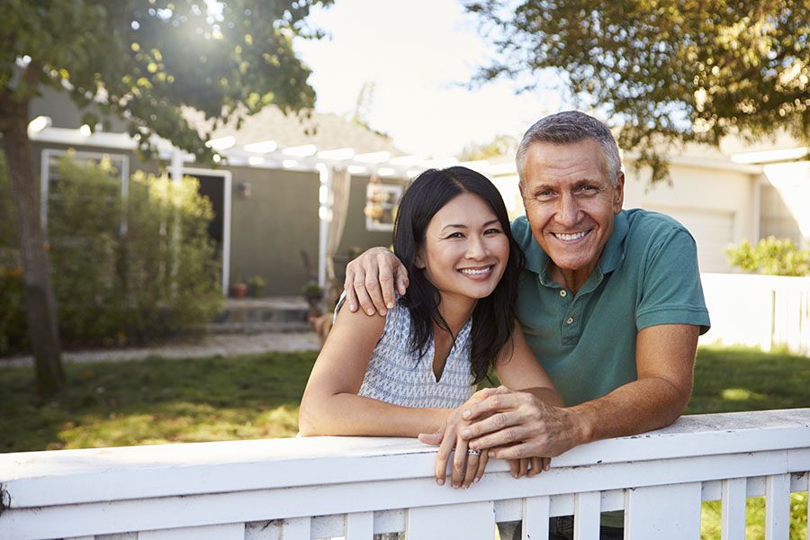 Homeowners Review Questionnaire - Portrait of Cheerful Couple Standing Next to a White Picket Fence in Their Backyard
